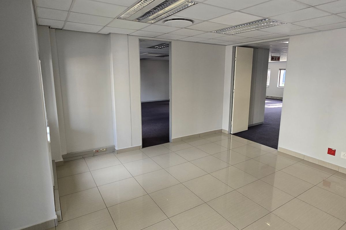 A bright, open-plan commercial office space featuring tiled flooring, recessed ceiling lighting, and neutral wall finishes, providing a clean and professional work environment.