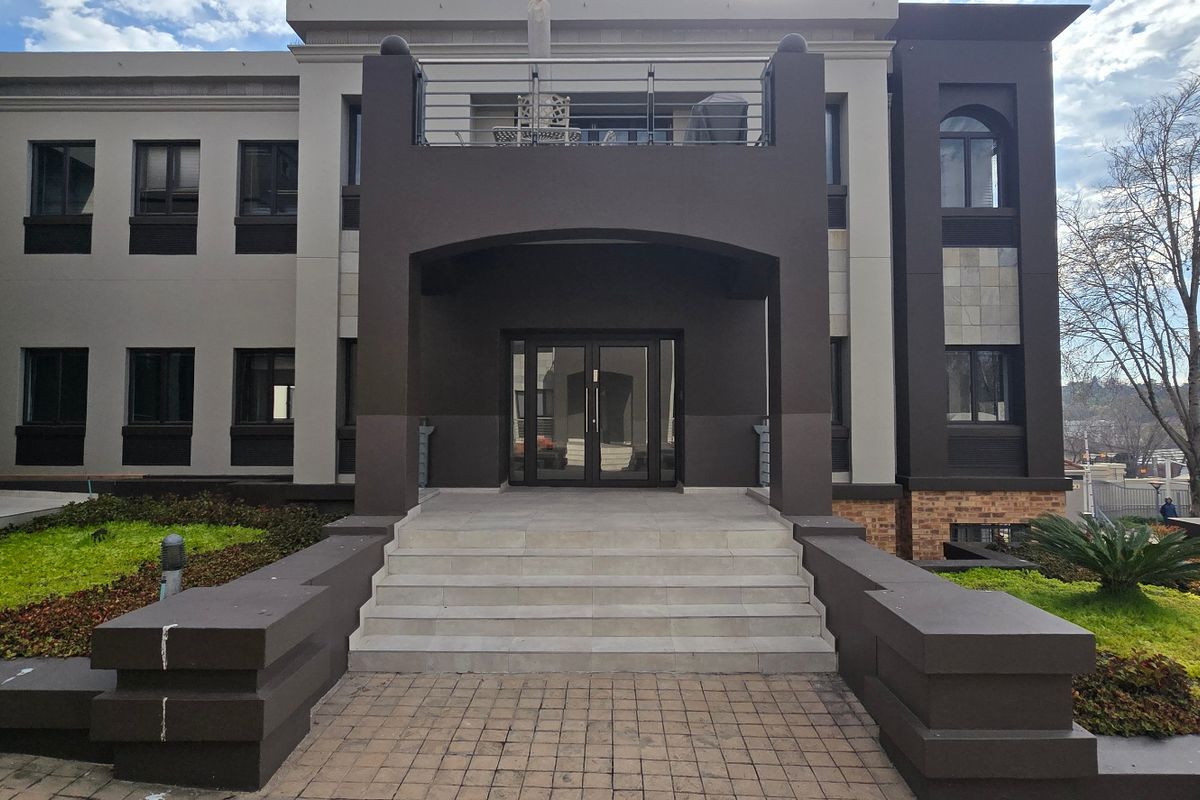 Modern commercial building exterior featuring a prominent entrance with stone steps, glass double doors, and a balcony above.