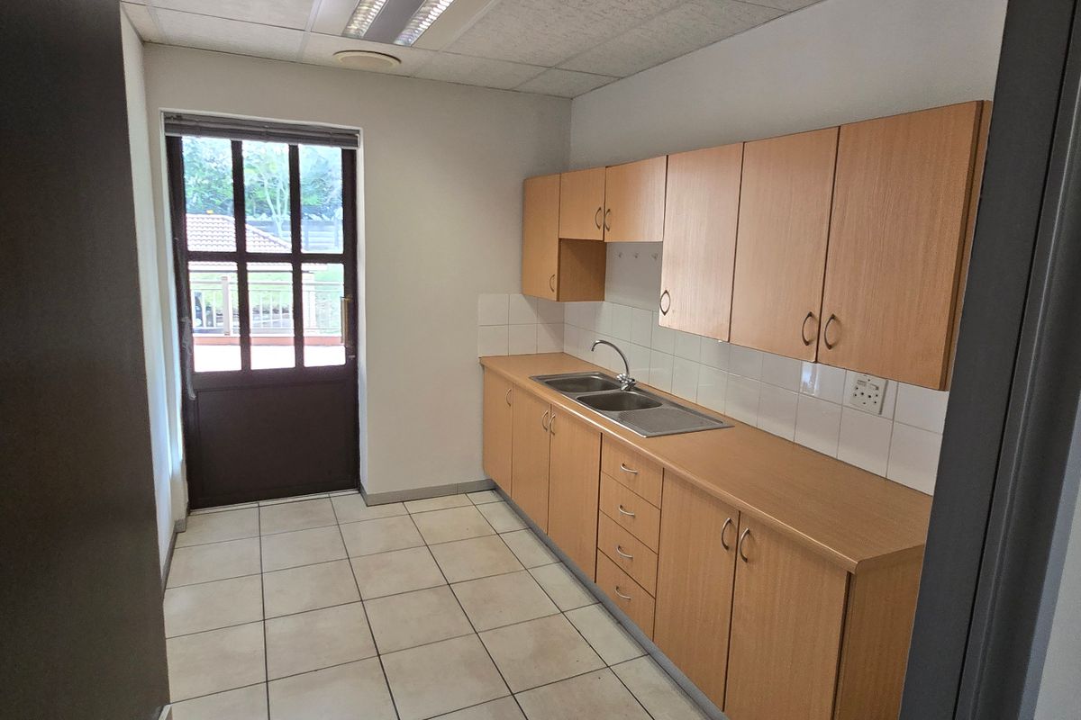A functional commercial kitchenette featuring light wood cabinetry, a stainless steel double sink, tiled flooring, and direct access to an outdoor area.