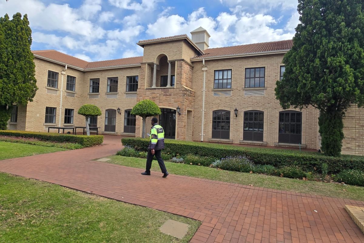 A well-maintained commercial building facade featuring face brick construction, tiled roofing, and landscaped garden areas with paved walkways.
