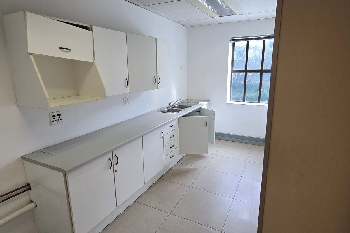 A functional kitchenette featuring white cabinetry, a double sink, tiled flooring, and a window, currently requiring minor repairs and cosmetic updates.