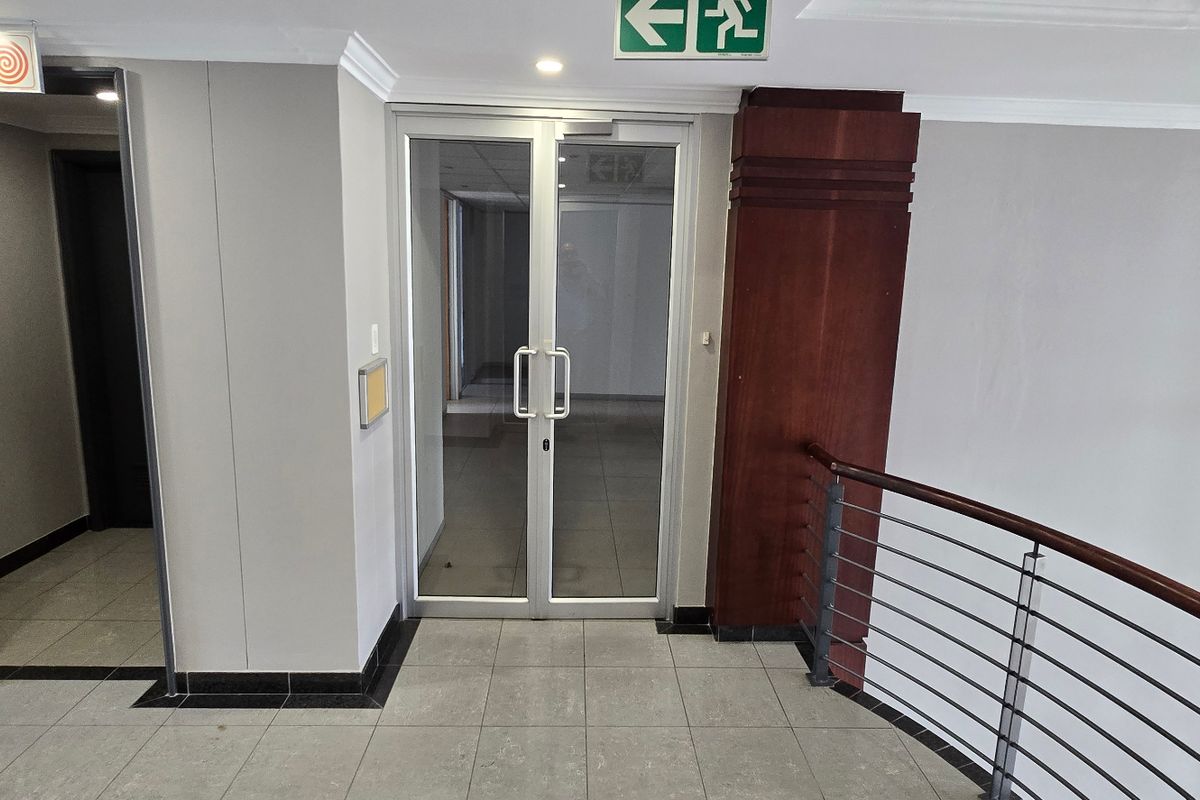 Commercial hallway featuring tiled flooring, glass double doors, and a wooden balustrade with metal railings.