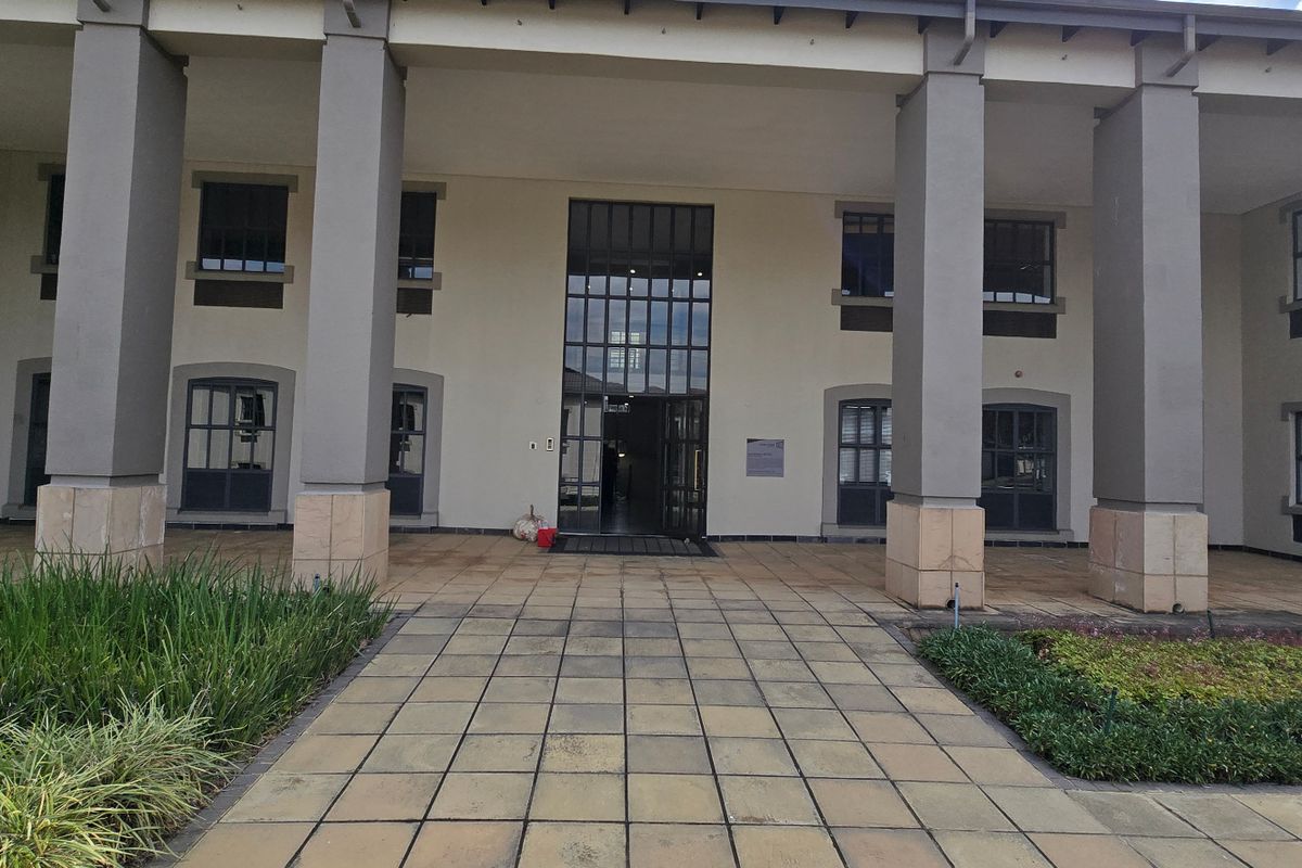 A professional commercial building entrance featuring a paved walkway, large structural pillars, and a glass-paneled doorway.