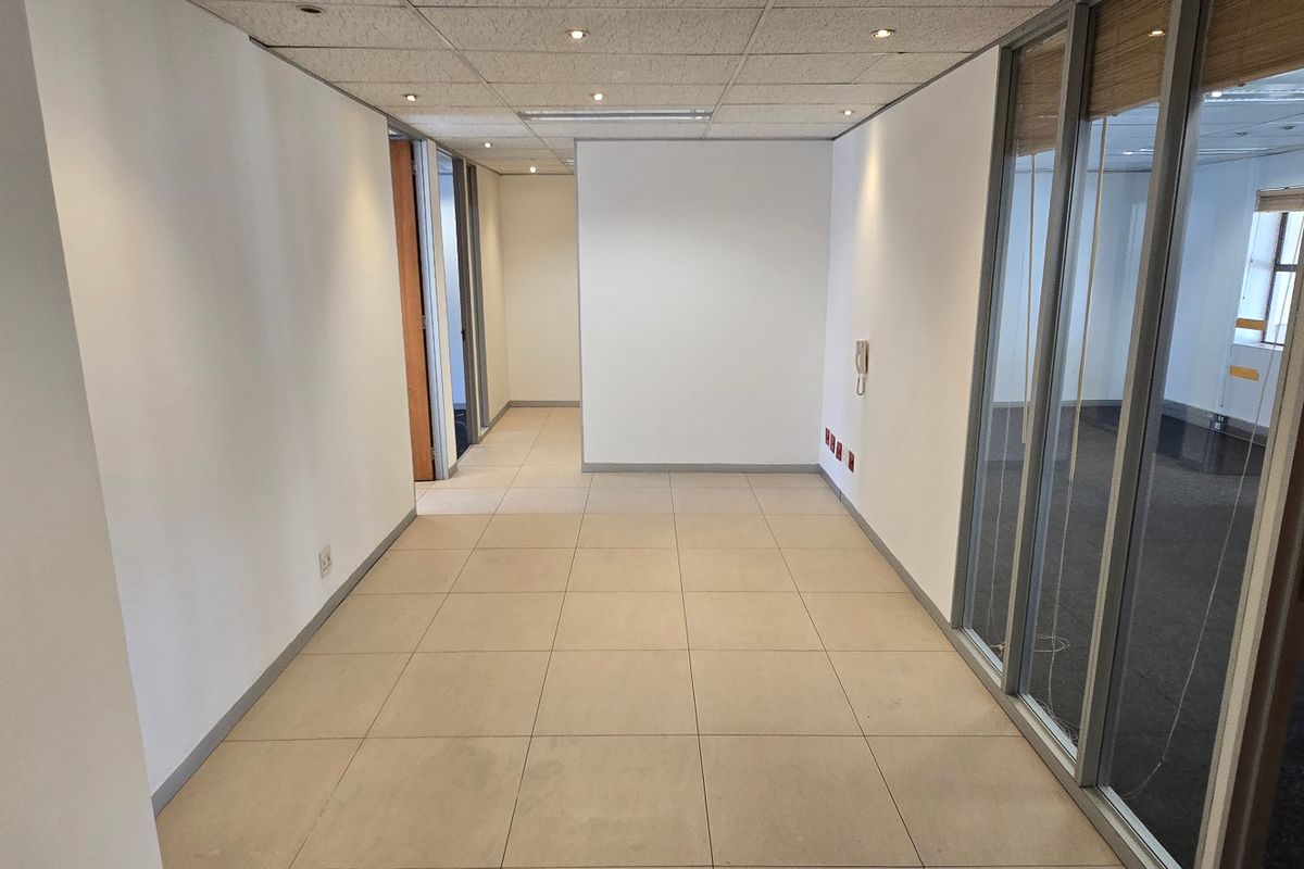 A vacant commercial office space featuring tiled flooring, recessed ceiling lighting, and glass partition walls, offering a clean and functional layout for business operations.