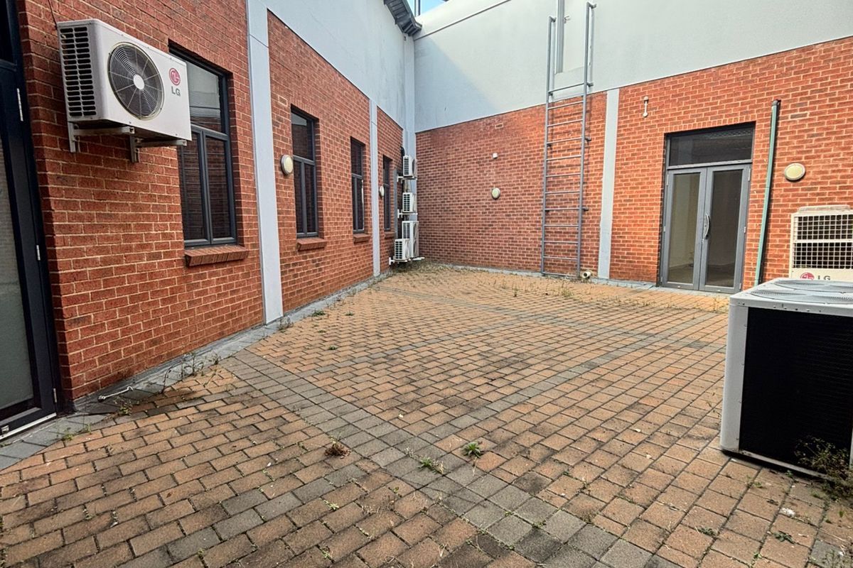 A paved rear courtyard area featuring exposed brick walls, multiple external air conditioning units, and a fixed metal access ladder.