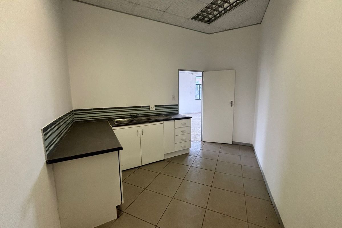 A functional kitchenette area featuring built-in cabinetry, a sink, and tiled flooring, suitable for office or commercial use.