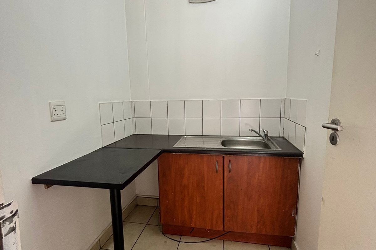 A compact kitchenette area featuring a single sink, built-in wooden cabinetry, tiled splashback, and an integrated counter extension.