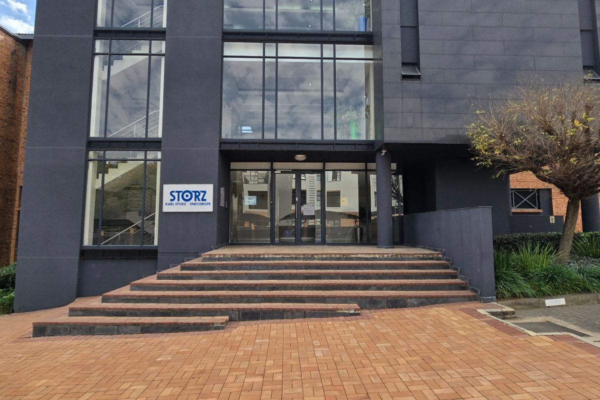 Modern commercial building entrance featuring a glass facade, dark stone cladding, and paved front access steps.