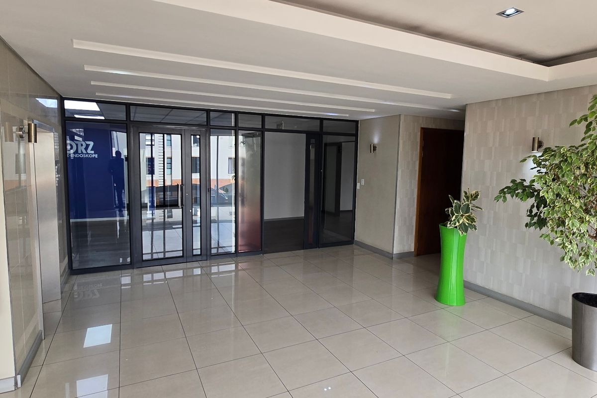 A bright and modern commercial entrance lobby featuring tiled flooring, recessed ceiling lighting, and glass-paneled office partitions.
