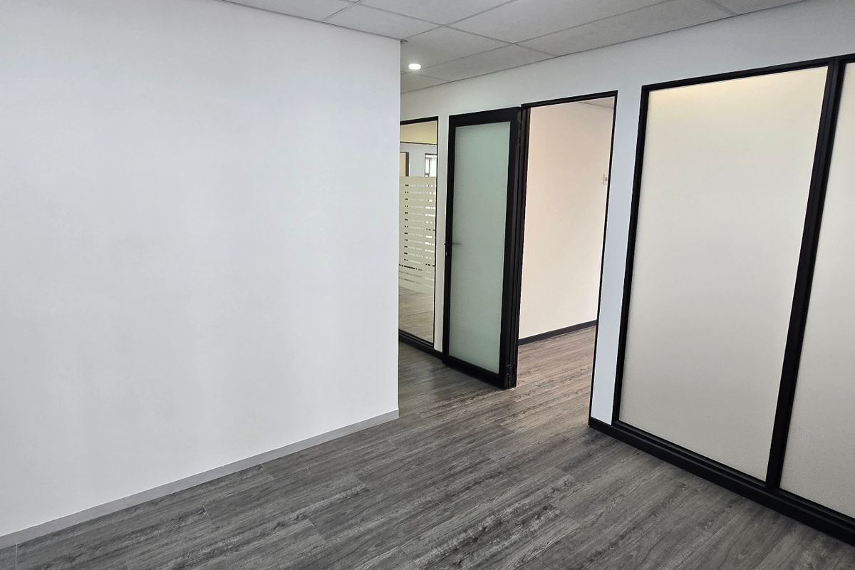 A modern, empty office space featuring dark wood-look flooring, black-framed glass partitions, and a suspended ceiling, offering a clean and professional commercial environment.