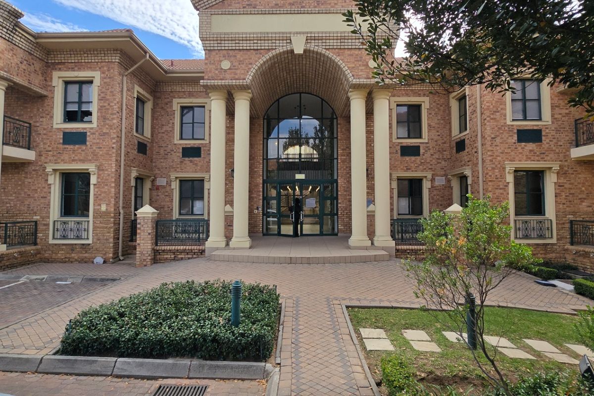 A professional commercial office building featuring a classic brick facade, grand arched entrance with columns, and paved courtyard area.