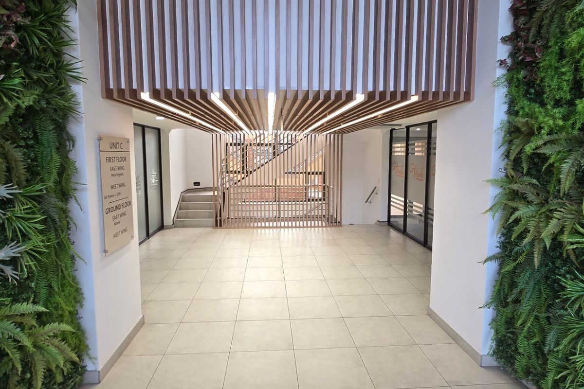 Modern commercial building entrance lobby featuring vertical timber slat ceiling detailing, tiled flooring, and integrated vertical garden walls.