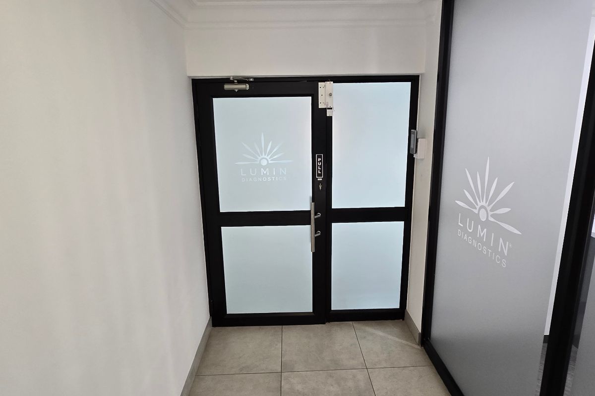 A professional commercial entrance featuring modern glass doors with frosted privacy film and branded signage, leading into a clean, tiled reception area.