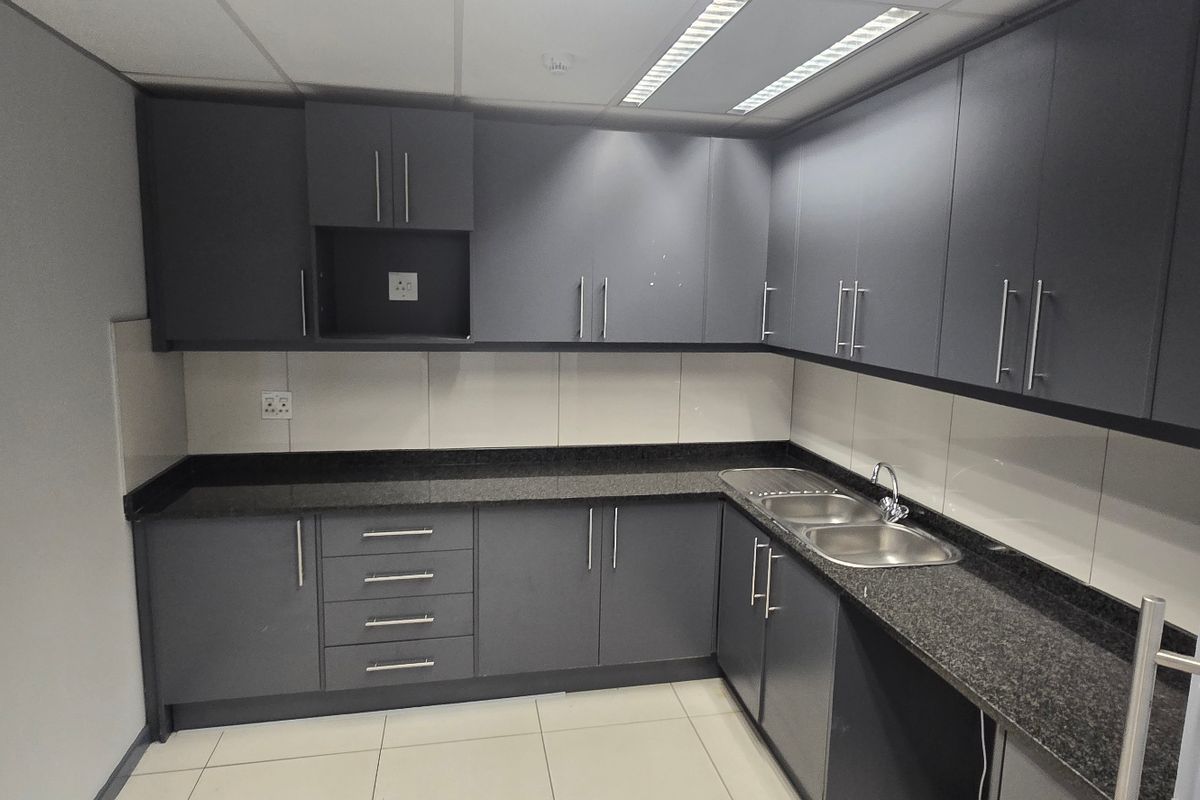 A modern commercial kitchenette featuring dark grey cabinetry, granite countertops, a double stainless steel sink, and tiled flooring.