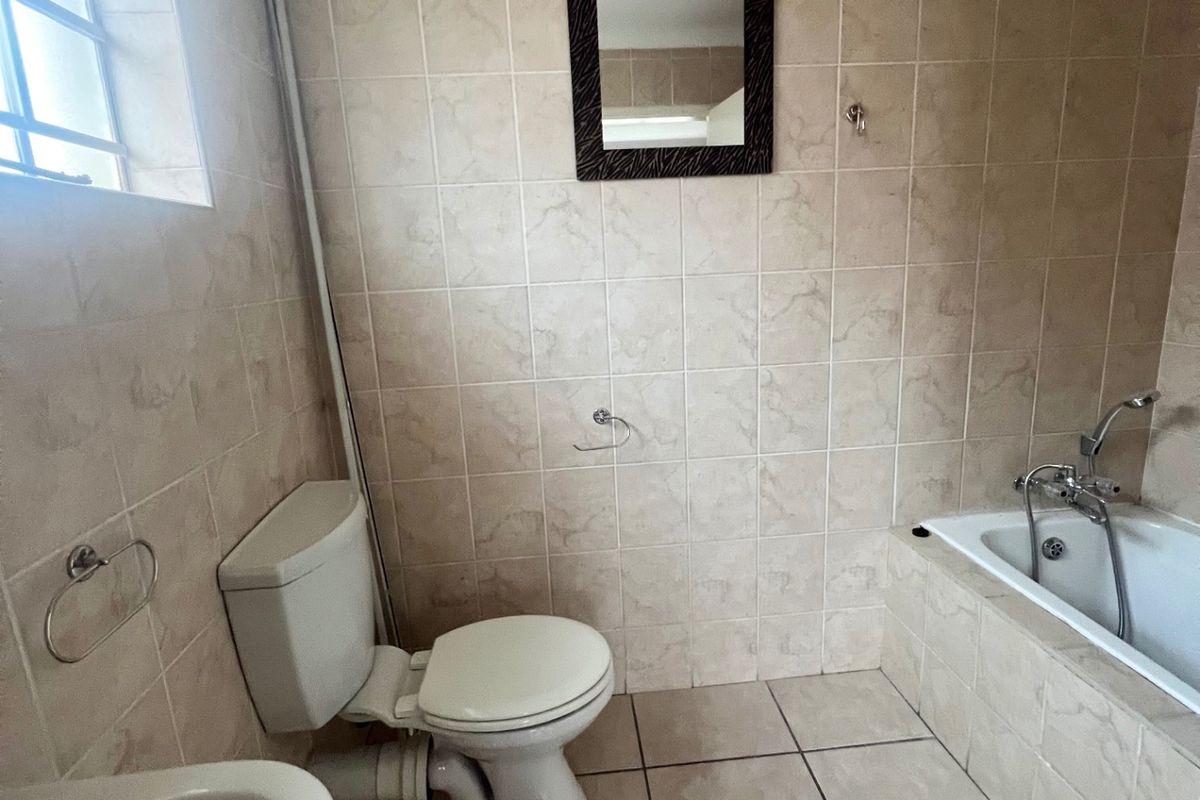A functional bathroom featuring tiled walls and flooring, a built-in bathtub with shower mixer, a toilet, and a wall-mounted basin.
