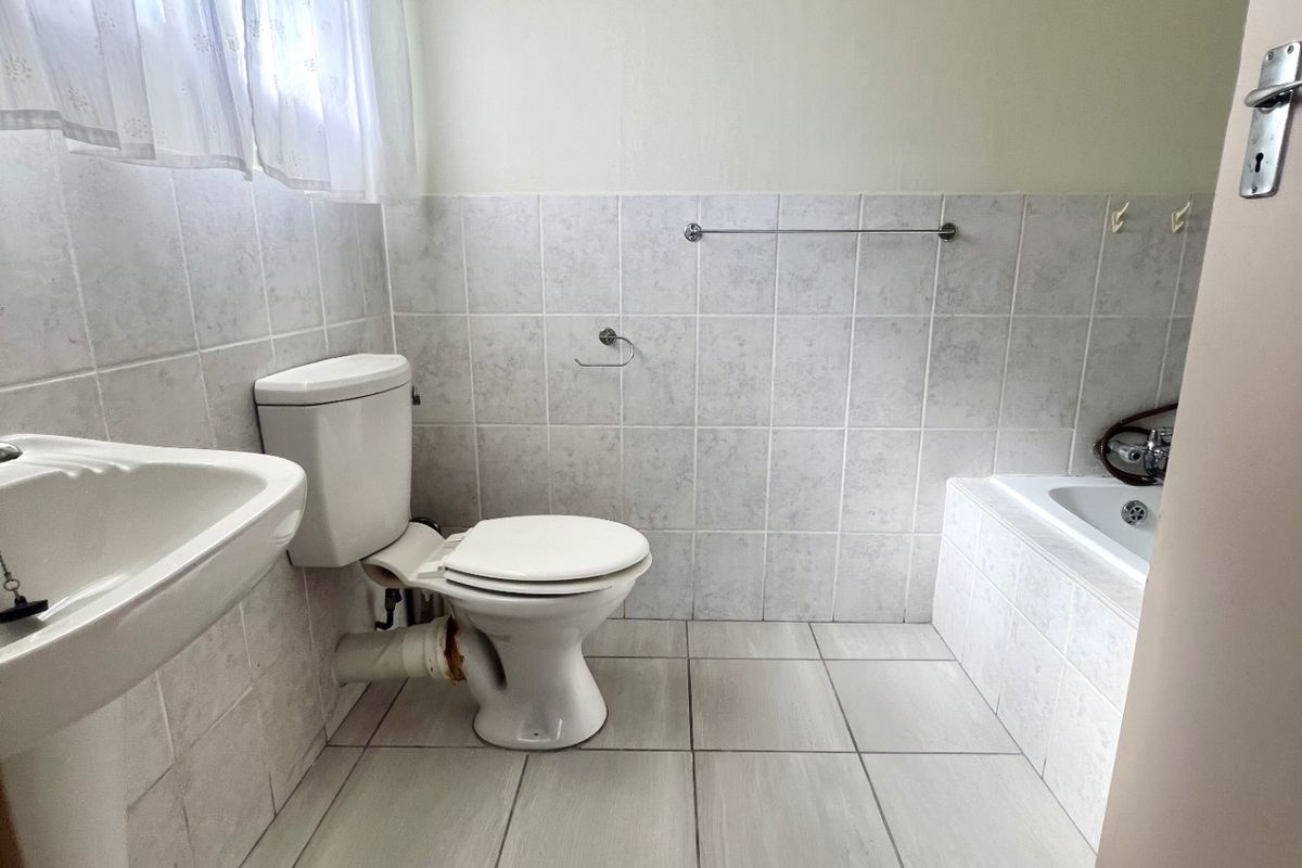 A functional bathroom featuring a pedestal basin, standard toilet, and a tiled bathtub with wall-mounted fixtures.
