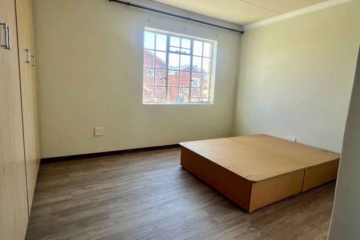 A bedroom featuring wood-look laminate flooring, built-in cupboards, and a large window providing natural light.