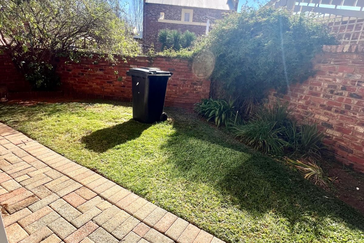 A private rear garden featuring a paved patio area, a well-maintained lawn, and perimeter brick boundary walls with security fencing.