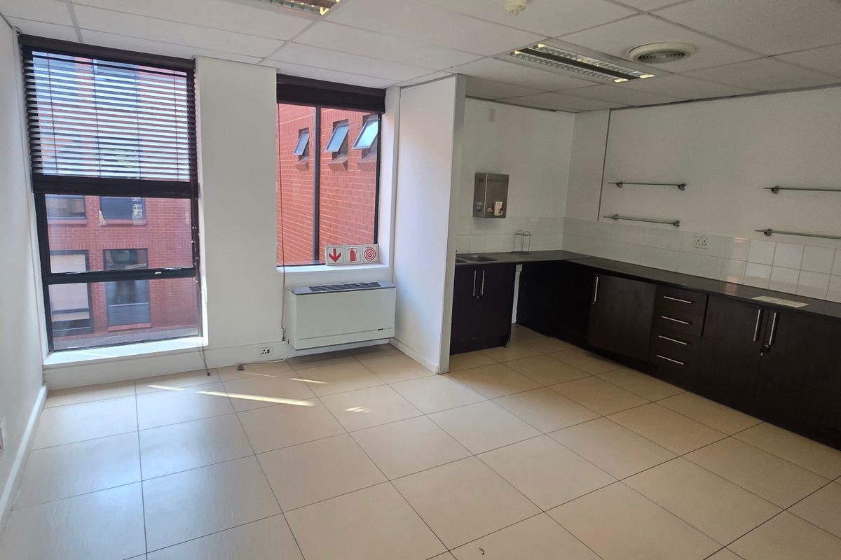 A functional commercial kitchenette area featuring dark cabinetry, tiled flooring, suspended ceiling, and large windows providing natural light.