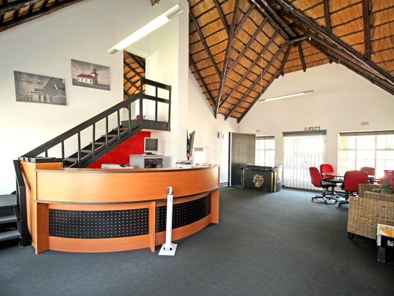 Spacious open-plan area featuring a high exposed thatch ceiling, a built-in reception desk, and a staircase leading to an upper level.