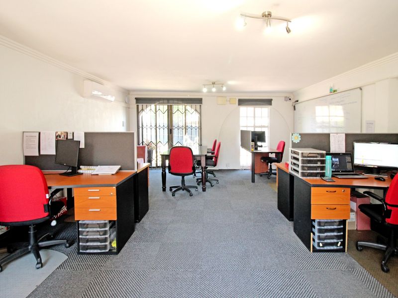 A functional office space featuring carpeted flooring, a wall-mounted air conditioning unit, and a security gate leading to the exterior.