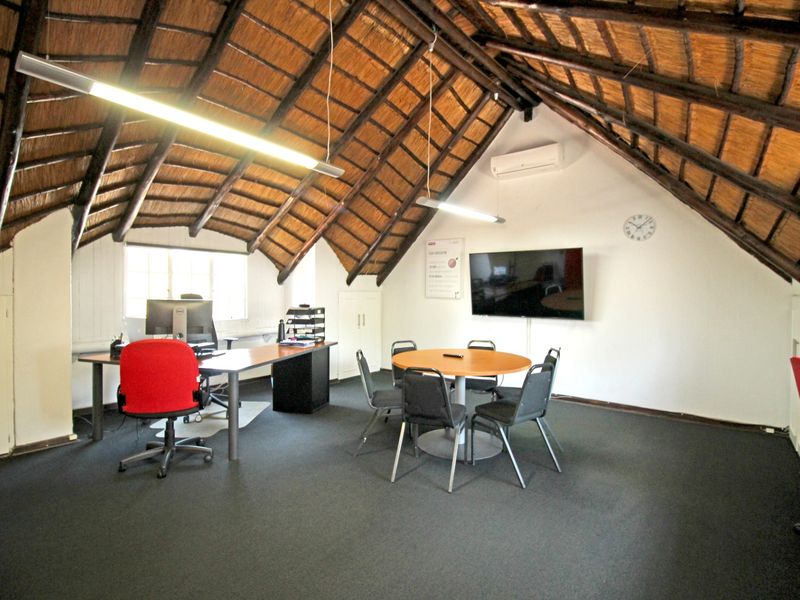 Spacious office area featuring a high vaulted thatched roof with exposed timber rafters and a wall-mounted air conditioning unit.