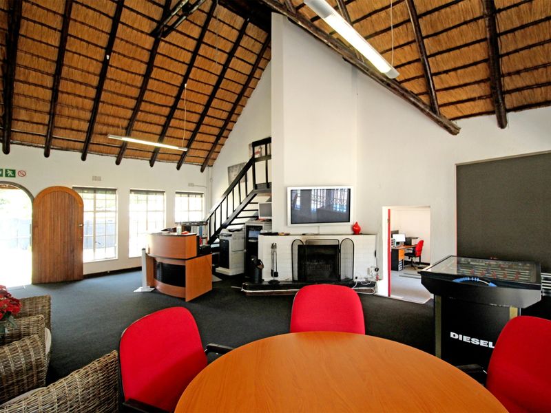 Spacious living area featuring a high vaulted thatched ceiling with exposed timber rafters, a central brick fireplace, and an internal staircase.