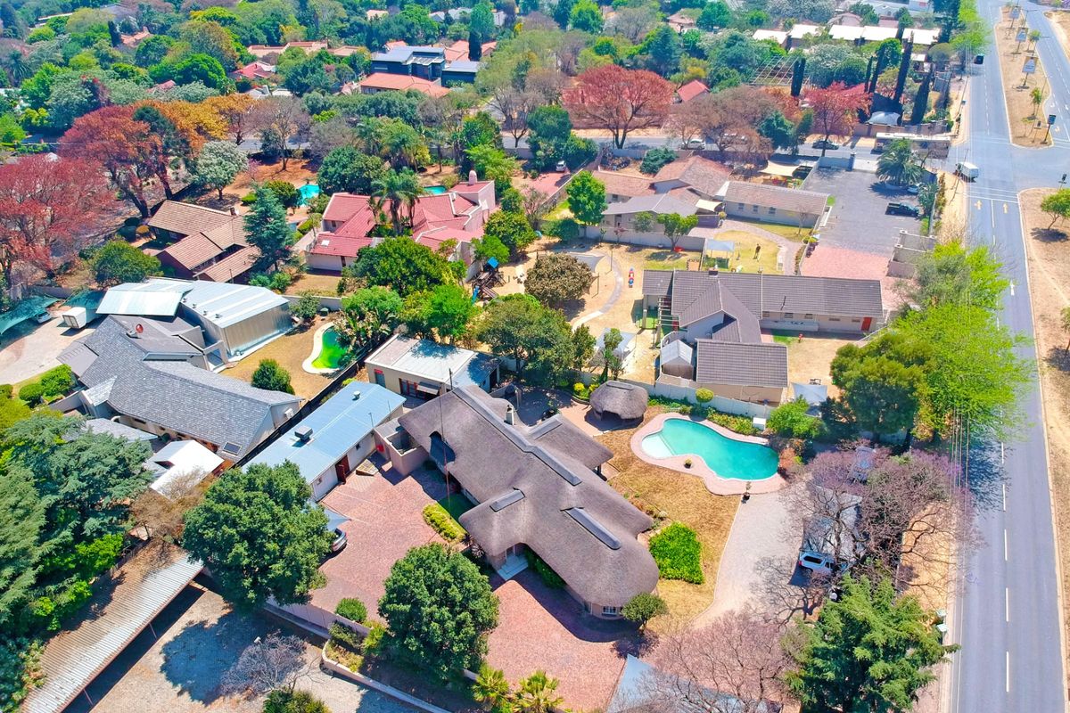 Aerial view of the property showcasing the main residence with a thatched roof, swimming pool, extensive paved driveway, and surrounding landscaped grounds.
