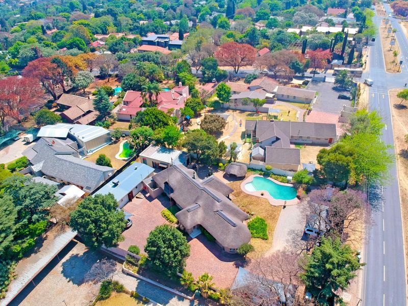 Aerial view of the property showcasing the main residence with a thatched roof, swimming pool, extensive paved driveway, and surrounding landscaped grounds.