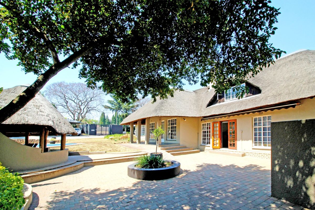 Spacious rear exterior featuring a traditional thatch roof, extensive paved patio area, and established garden surroundings.