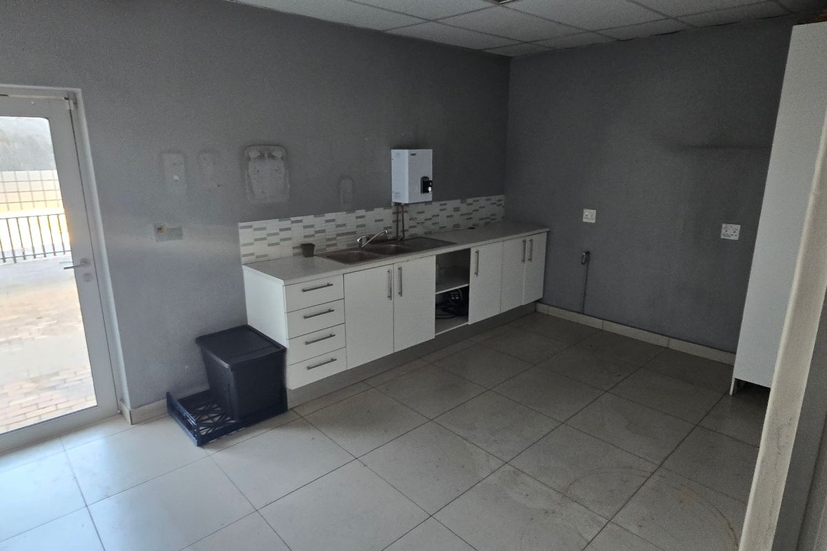 A functional kitchenette area featuring built-in cabinetry, a stainless steel sink, tiled splashback, and direct access to an outdoor patio area.