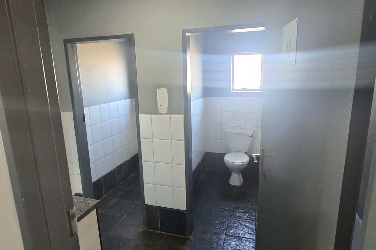 Functional industrial restroom facility featuring tiled walls, dark floor tiling, and standard sanitary fixtures.