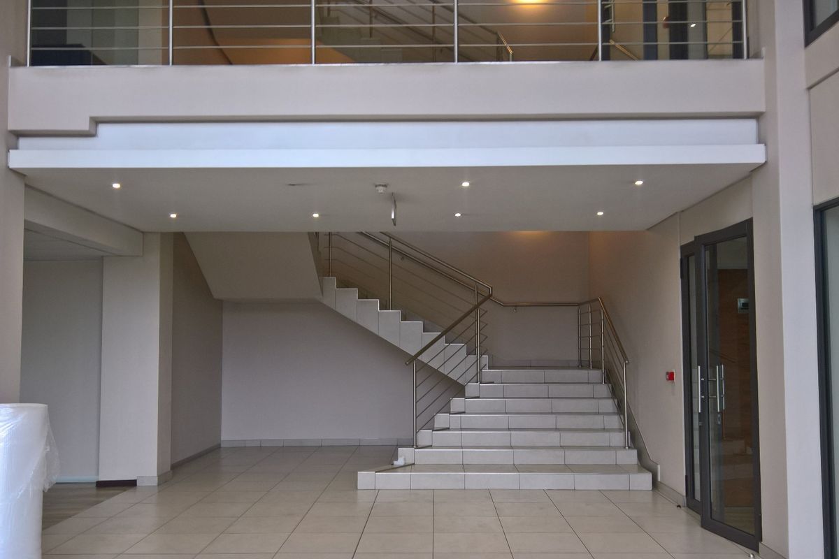 Spacious industrial entry foyer featuring a tiled staircase with stainless steel balustrades, recessed lighting, and a mezzanine level overlooking the main entrance area.