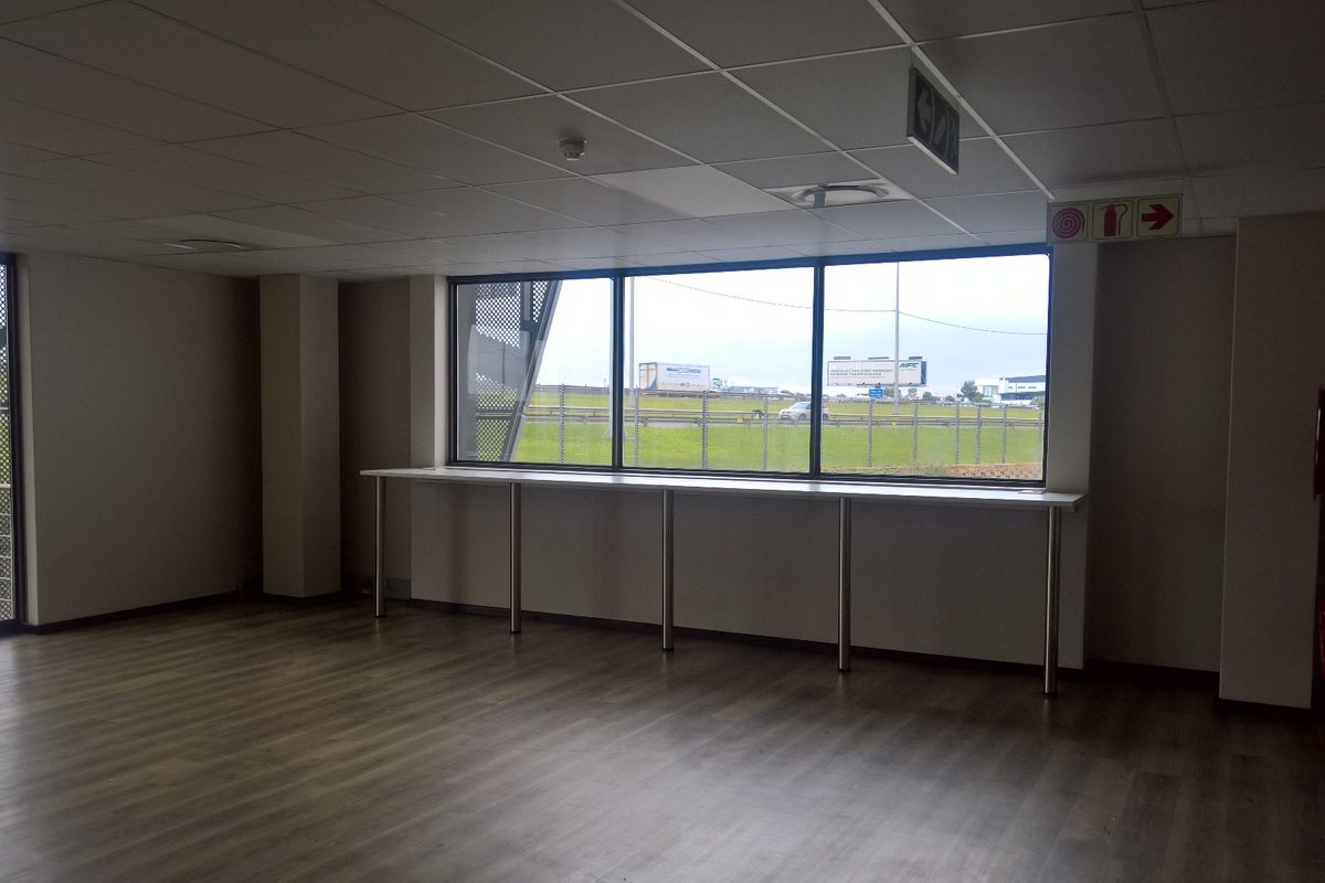 A bright, open-plan office space featuring laminate flooring, a suspended ceiling, and a built-in window counter with views of the surrounding industrial area.