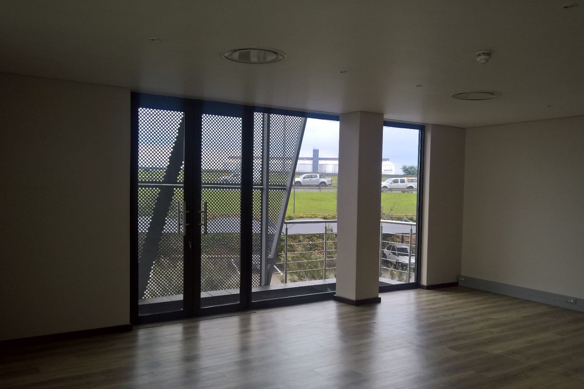 Spacious, modern office area featuring laminate flooring, recessed lighting, and large glass doors opening to a balcony with metal security screening.