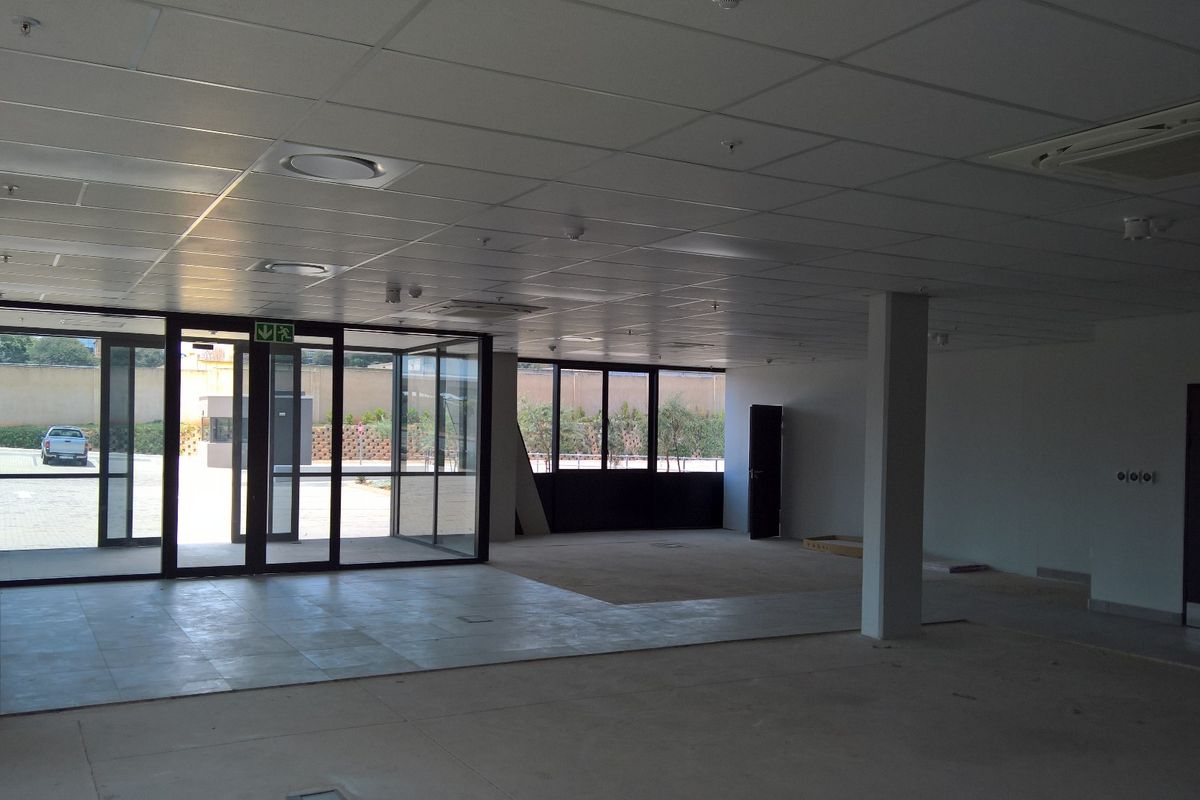 Spacious open-plan industrial office area featuring large glass doors, suspended ceilings, and integrated air conditioning, offering a versatile and well-lit workspace.