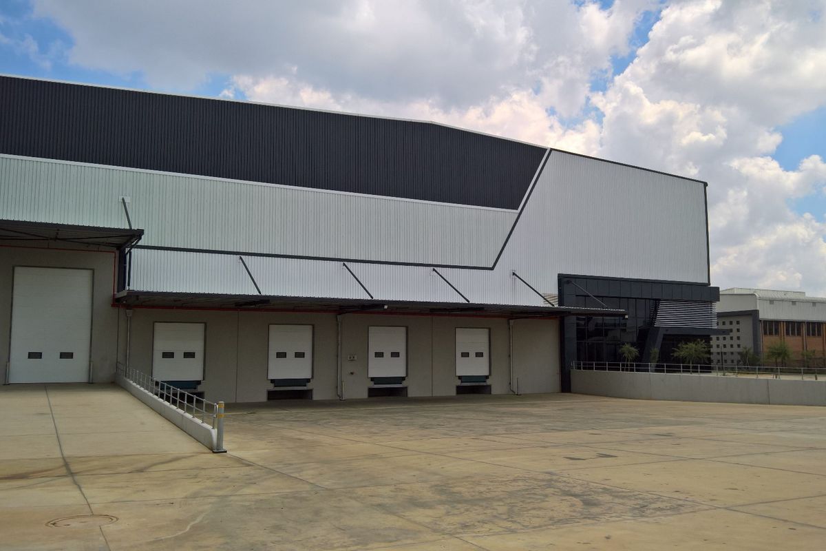 Industrial warehouse exterior featuring multiple loading docks with roller shutter doors, a concrete loading apron, and modern metal cladding.