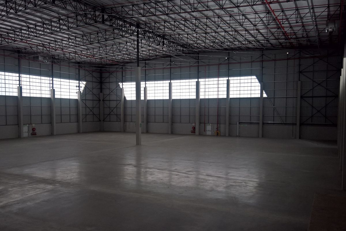 Spacious industrial warehouse featuring high ceilings with exposed steel trusses, polished concrete flooring, and integrated fire sprinkler systems.