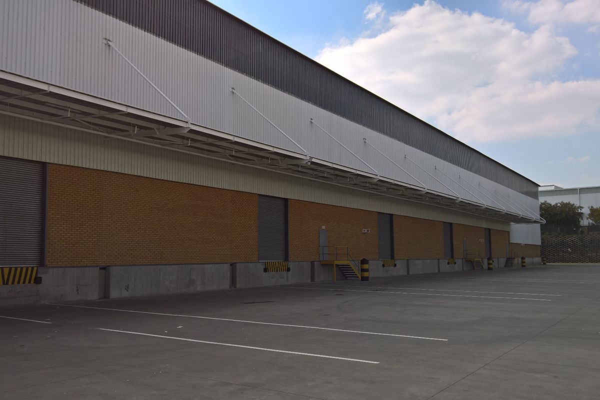 Industrial warehouse exterior featuring multiple roller shutter loading bays, concrete hardstand area, and steel canopy structure.