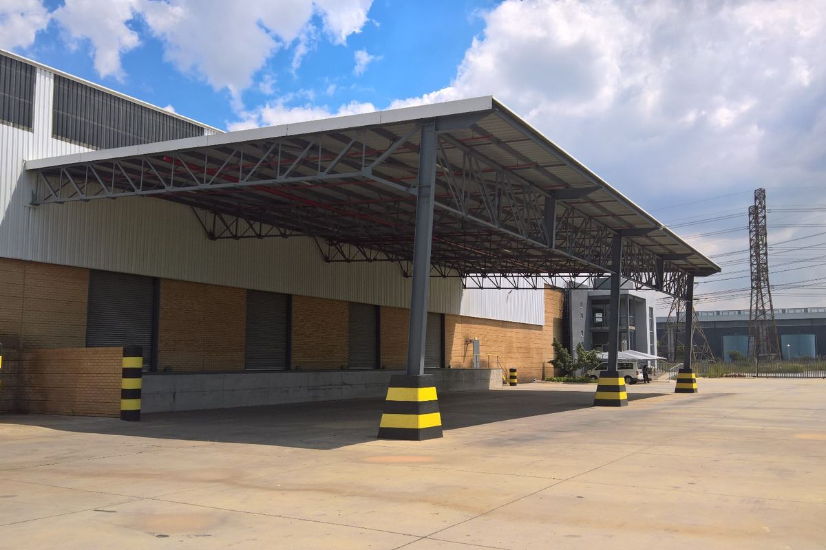 Industrial loading area featuring a large steel canopy, concrete hardstand, and multiple roller shutter doors for efficient logistics and freight operations.
