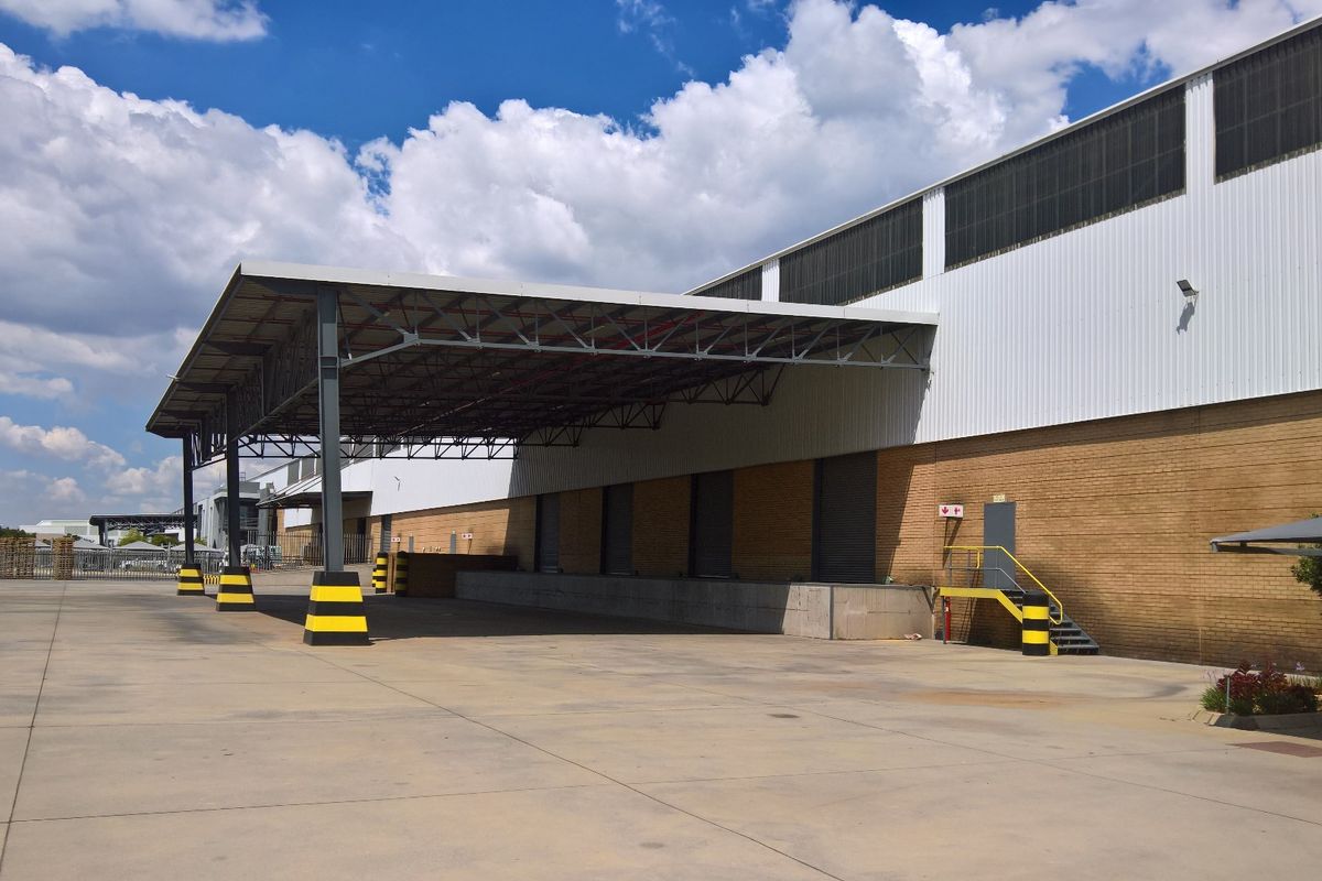 Industrial warehouse exterior featuring a large covered loading bay, concrete apron, and brick facade with metal cladding.
