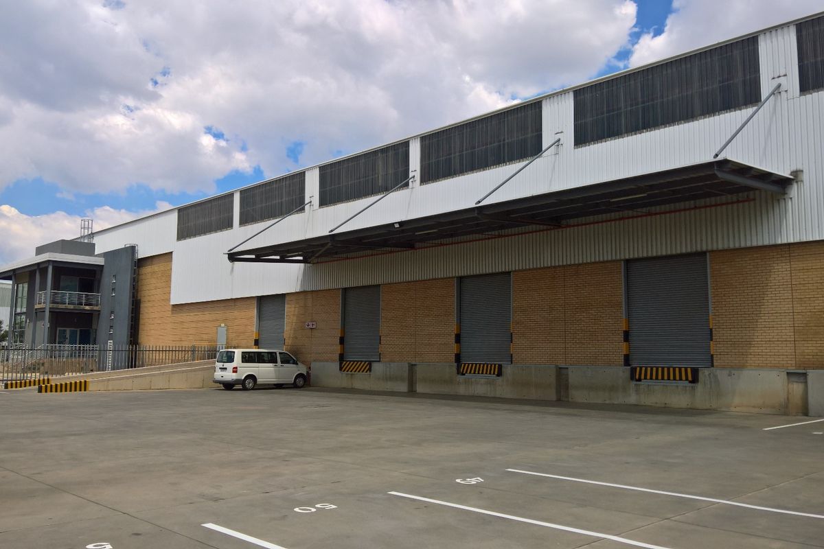 Industrial warehouse exterior featuring multiple roller shutter doors, a dedicated loading bay, and a spacious concrete yard area.