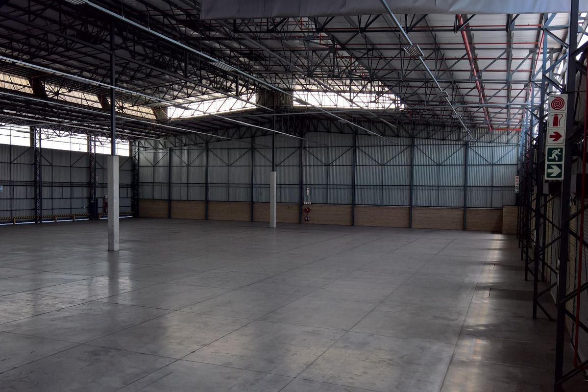 Spacious industrial warehouse featuring high-clearance steel truss roofing, polished concrete flooring, and durable corrugated metal wall cladding with integrated fire safety equipment.