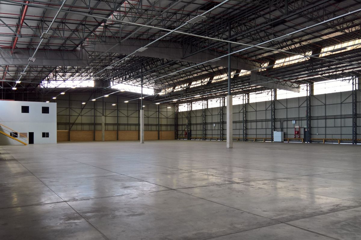 Expansive industrial warehouse space featuring high ceilings with exposed steel trusses, polished concrete flooring, and an integrated mezzanine office area.