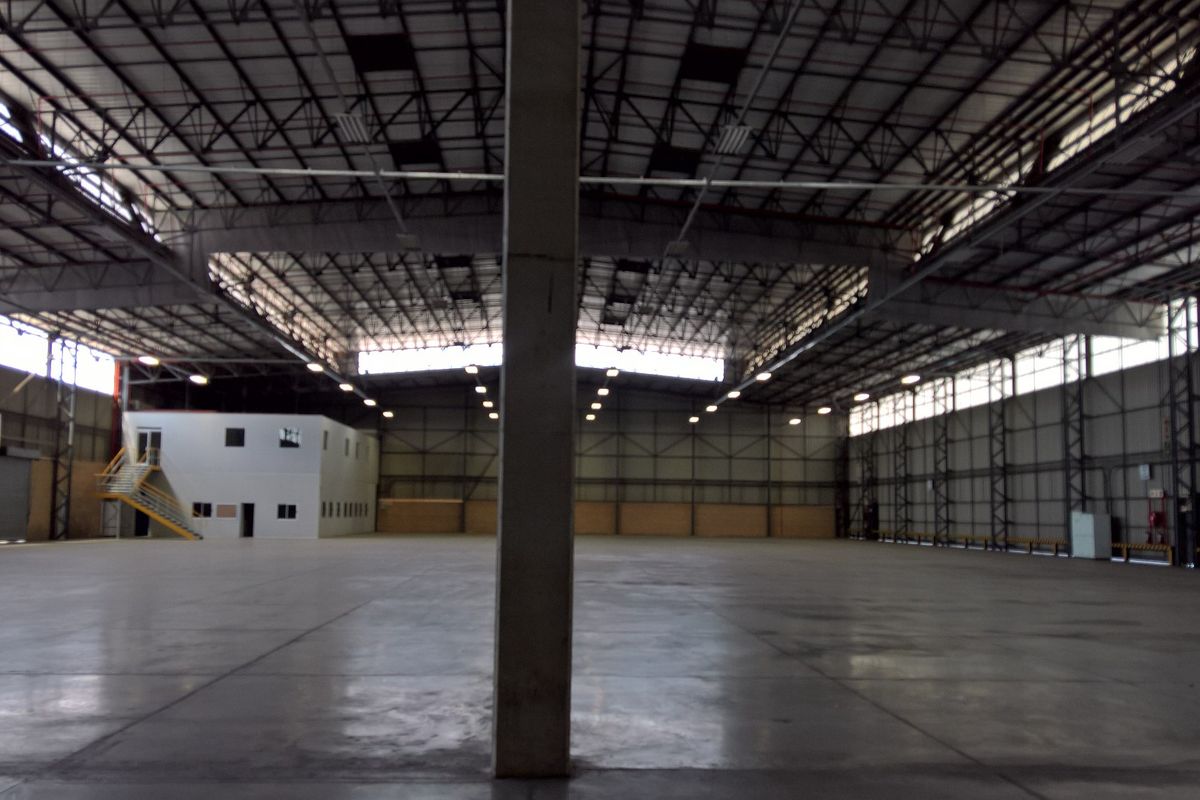 Expansive industrial warehouse space featuring high ceilings, polished concrete flooring, steel truss roofing, and an integrated two-story office block.