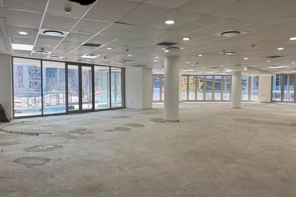 Spacious open-plan commercial office area featuring large glass windows, structural columns, and a suspended ceiling, currently in a shell condition ready for fit-out.