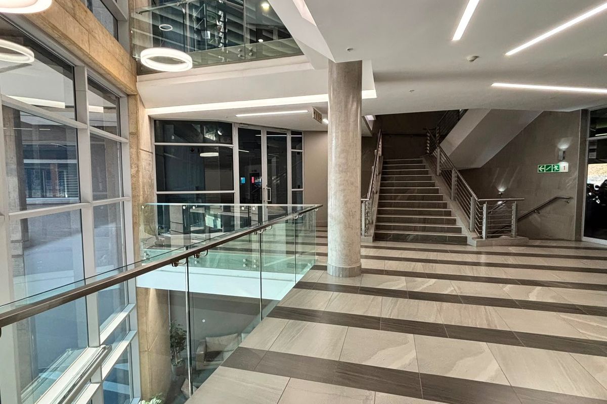 Modern commercial building entrance lobby featuring a grand staircase, glass balustrades, and high-quality tiled flooring with extensive natural light from full-height glazing.
