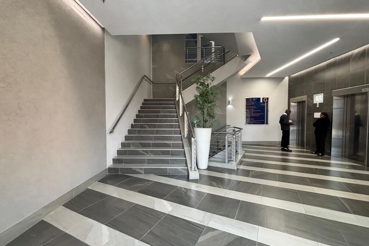 Modern commercial building lobby featuring a tiled staircase, stainless steel handrails, elevator access, and contemporary stone wall finishes.