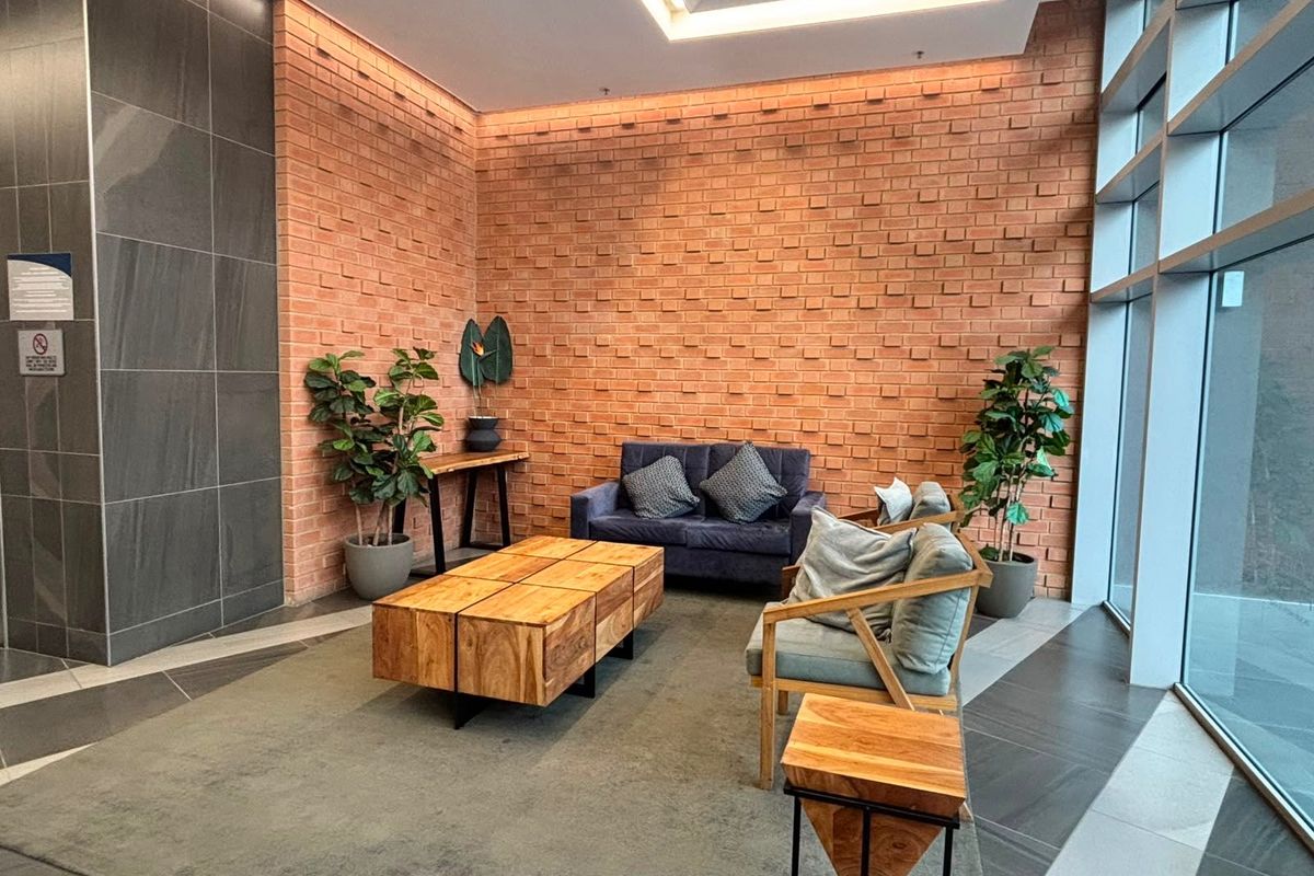 Modern commercial lobby or waiting area featuring an exposed brick feature wall, large format floor tiles, and expansive floor-to-ceiling windows providing natural light.