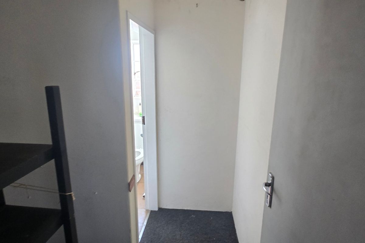 A narrow interior hallway with plain walls and flooring, leading towards an adjacent room.